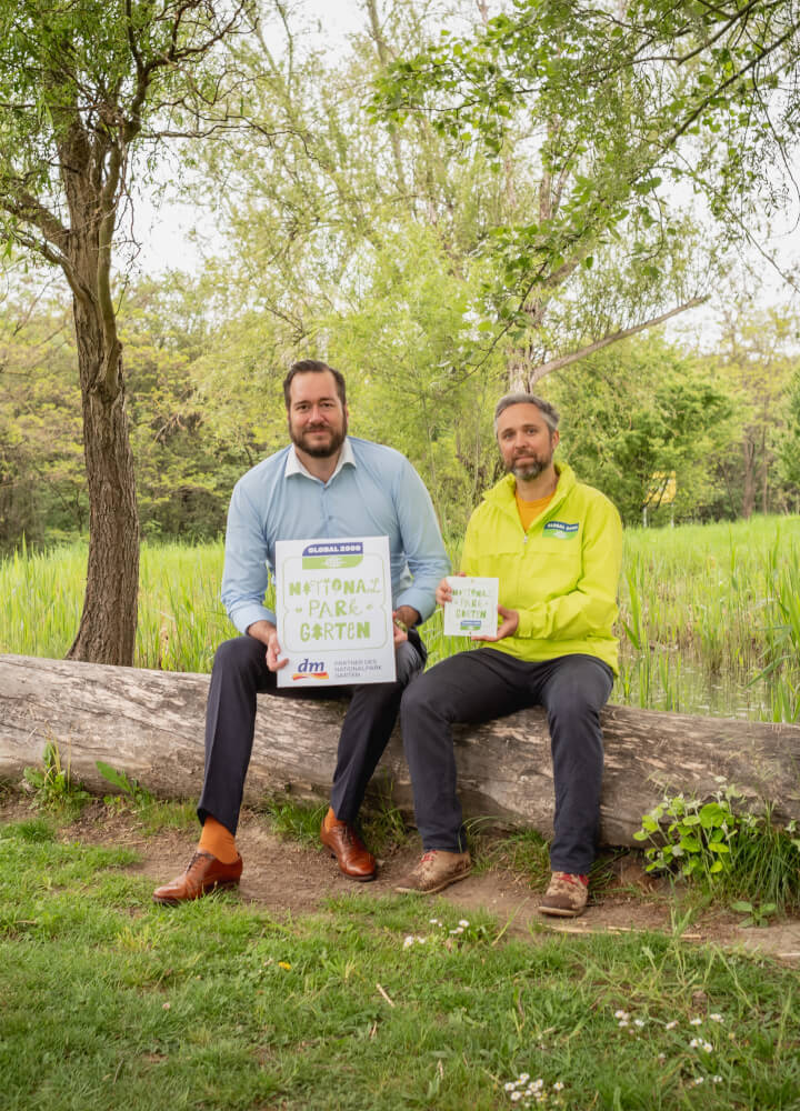 dm-Geschäftsführer Harald Bauer und Biodiversitätsexperte Dominik Linhard von GLOBAL 2000 halten eine Plakette des Nationalpark Garten in der Hand.