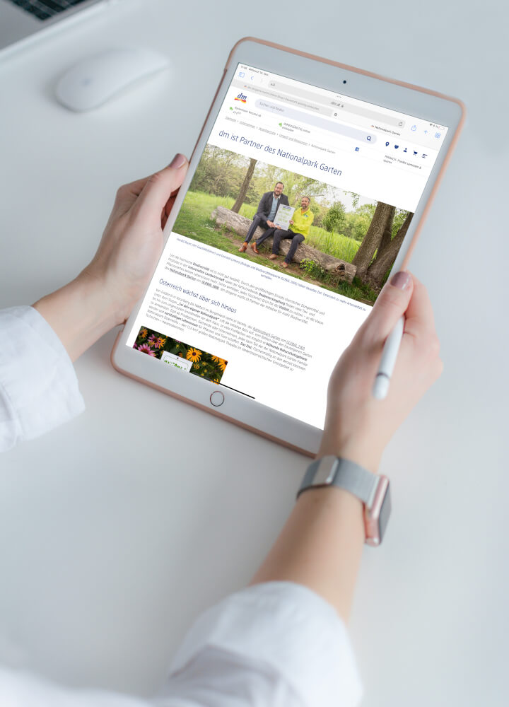 Hände halten ein Tablet, auf dem eine Website von dm angezeigt wird.