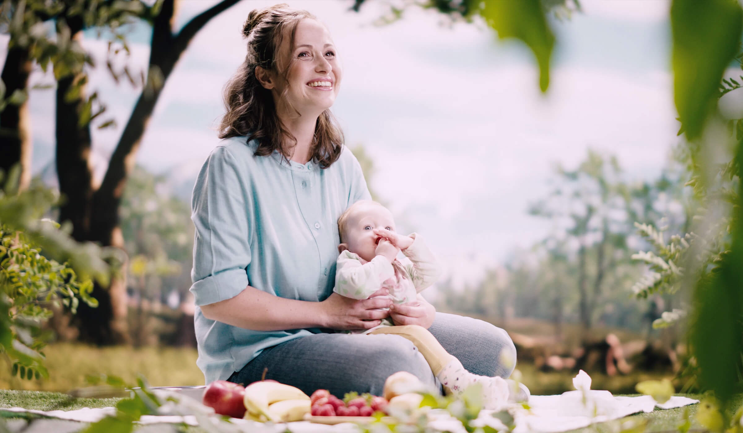 Frau sitzt mit Baby auf dem Arm auf einer Picknick-Decke.
