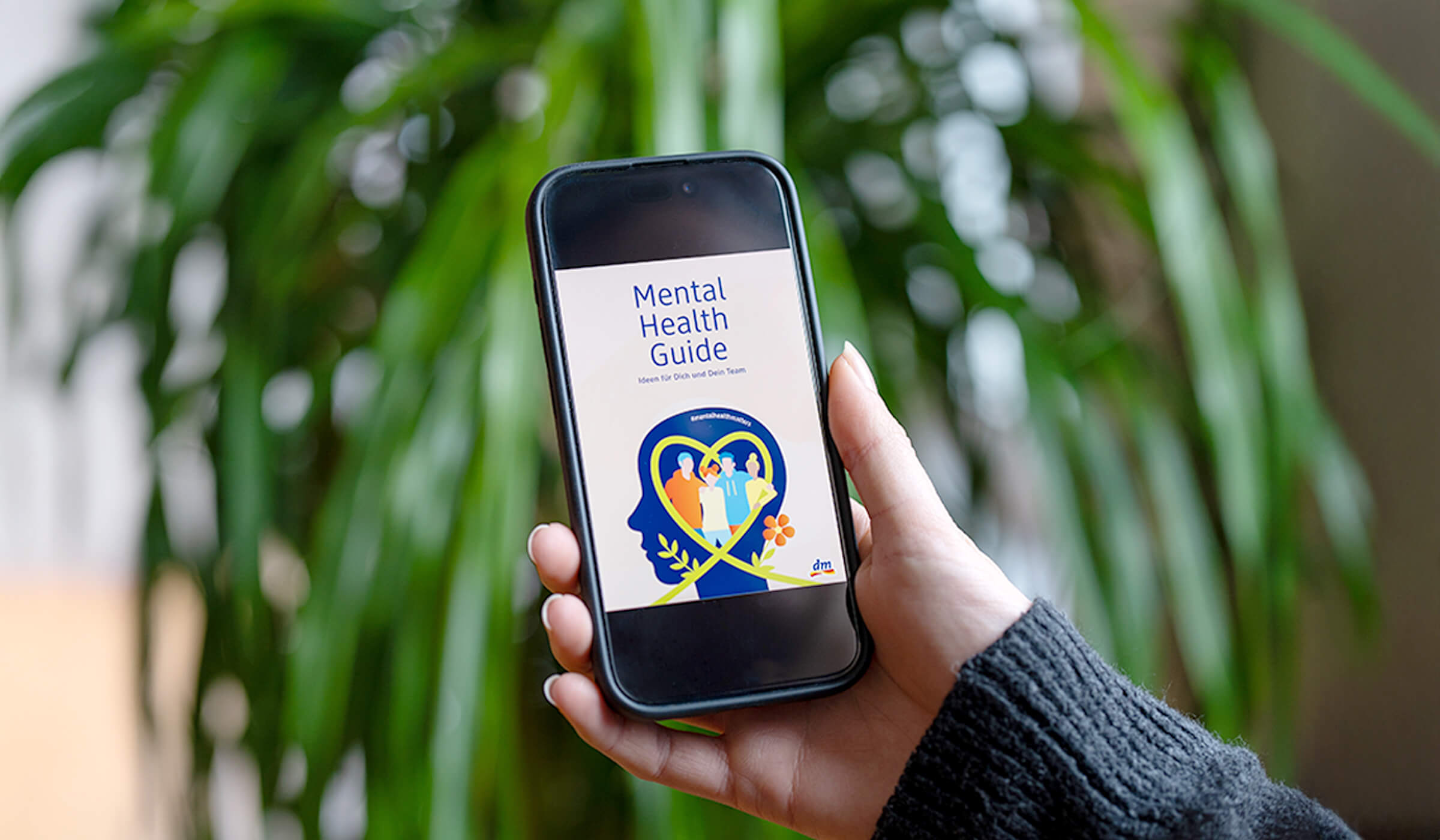 Hand hält ein Handy auf dem der Mental Health Guide zu sehen ist.