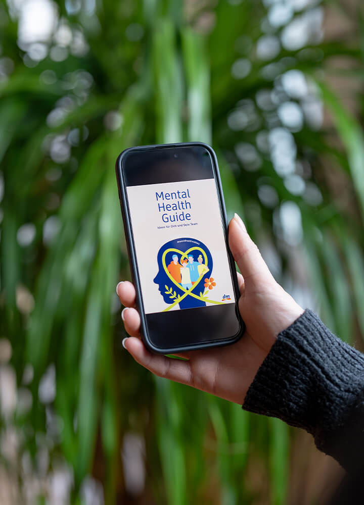 Hand hält ein Handy auf dem der Mental Health Guide zu sehen ist.